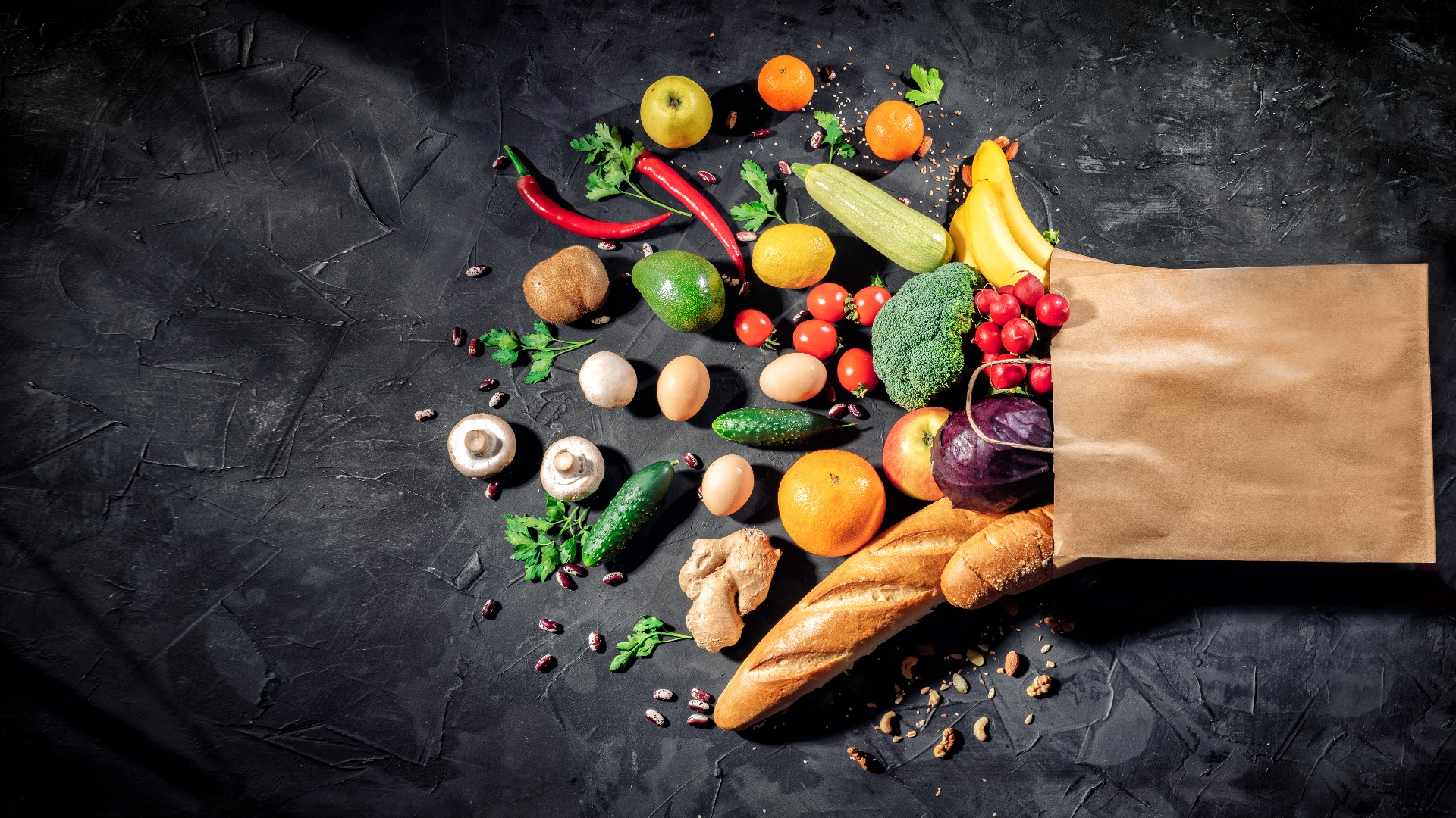 Gesundes Essen in voller Papiertüte mit verschiedenen Produkten Gemüse und Obst auf dunklem Hintergrund